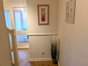 Un pasillo con piso de madera, una planta en maceta y dos cuadros en la pared.