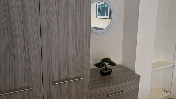 Ein Zimmer mit einem grauen Kleiderschrank, einer kleinen Kommode mit Bonsai-Baum und einem runden Spiegel an der Wand.