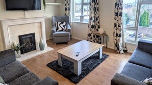 A living room with a fireplace, a television mounted on the wall, a grey armchair, a coffee table, and a sofa. - Theatre Severn Town House, Parking & Quarry Views (Shropshire)