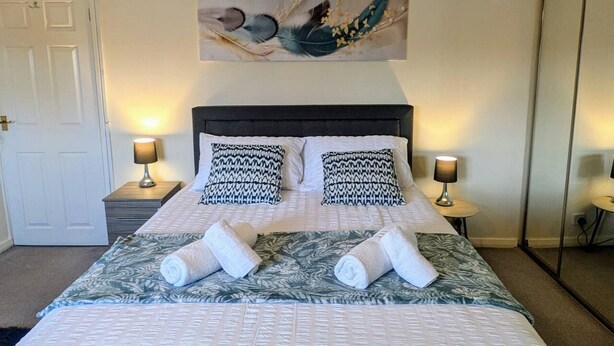 A hotel room with a bed, two bedside tables, a painting above the bed, and a door on the left. - Theatre Severn Town House, Parking & Quarry Views (Shropshire)