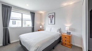 A hotel room with a large bed, a nightstand, a lamp, a picture on the wall, and a window with curtains. - 18 Jimmy (Lake Tekapo)