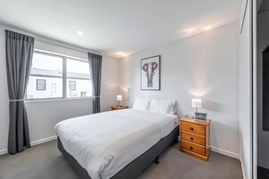 A hotel room with a large bed, a nightstand, a lamp, a picture on the wall, and a window with curtains.
