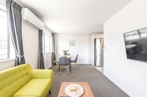 A modern living room with a sofa, a dining table with chairs, a coffee table, and a TV mounted on the wall.
