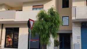 Un bâtiment moderne doté de nombreux balcons, d’un magasin bien visible appelé « Febolcasa Monopoli » et d’un panneau de signalisation triangulaire.
