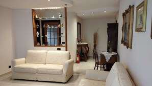 Un salon avec un canapé beige, un tapis à motifs et une vitrine en verre contenant des objets décoratifs.
