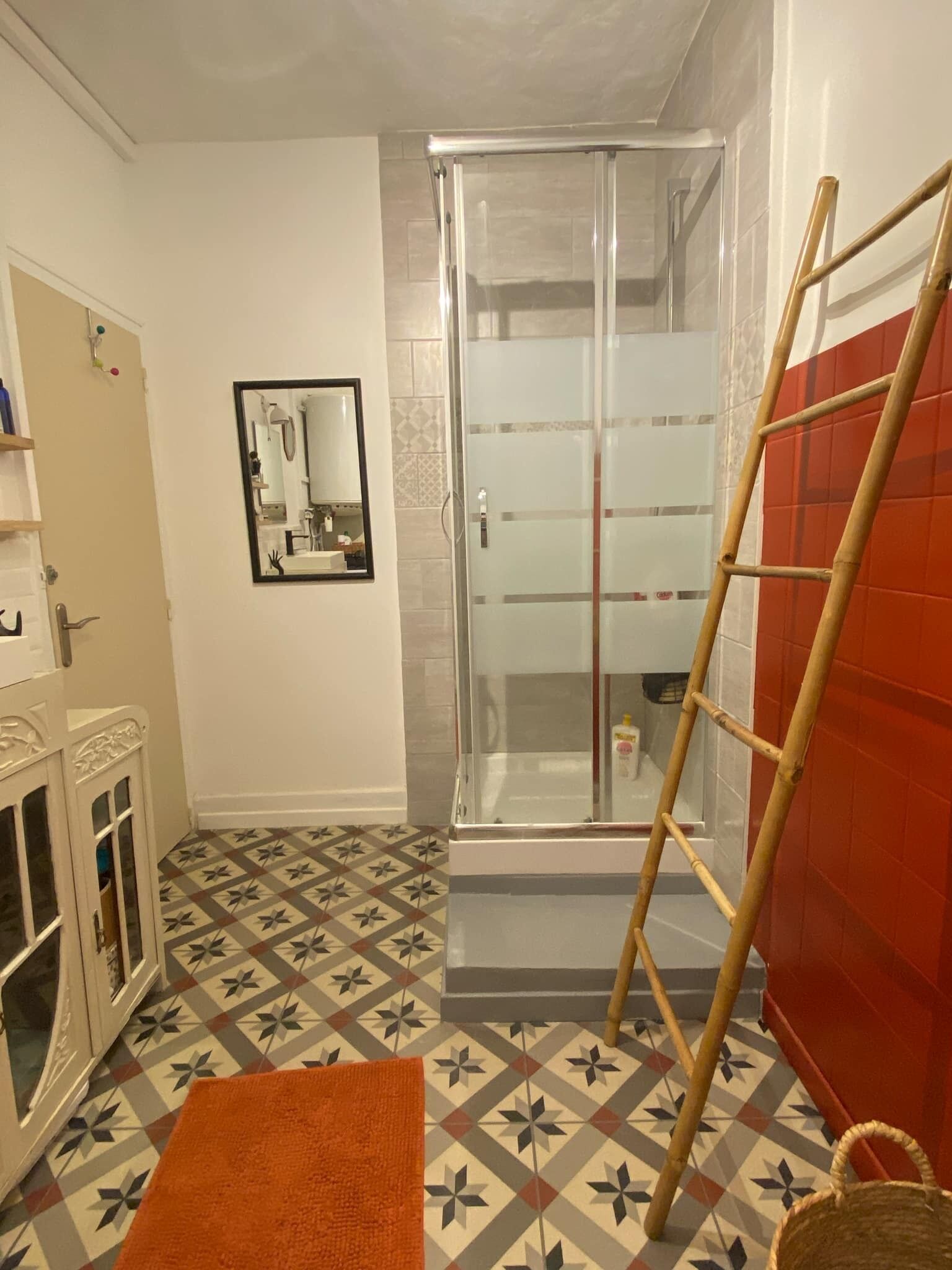 Un baño con ducha, espejo y piso estampado.