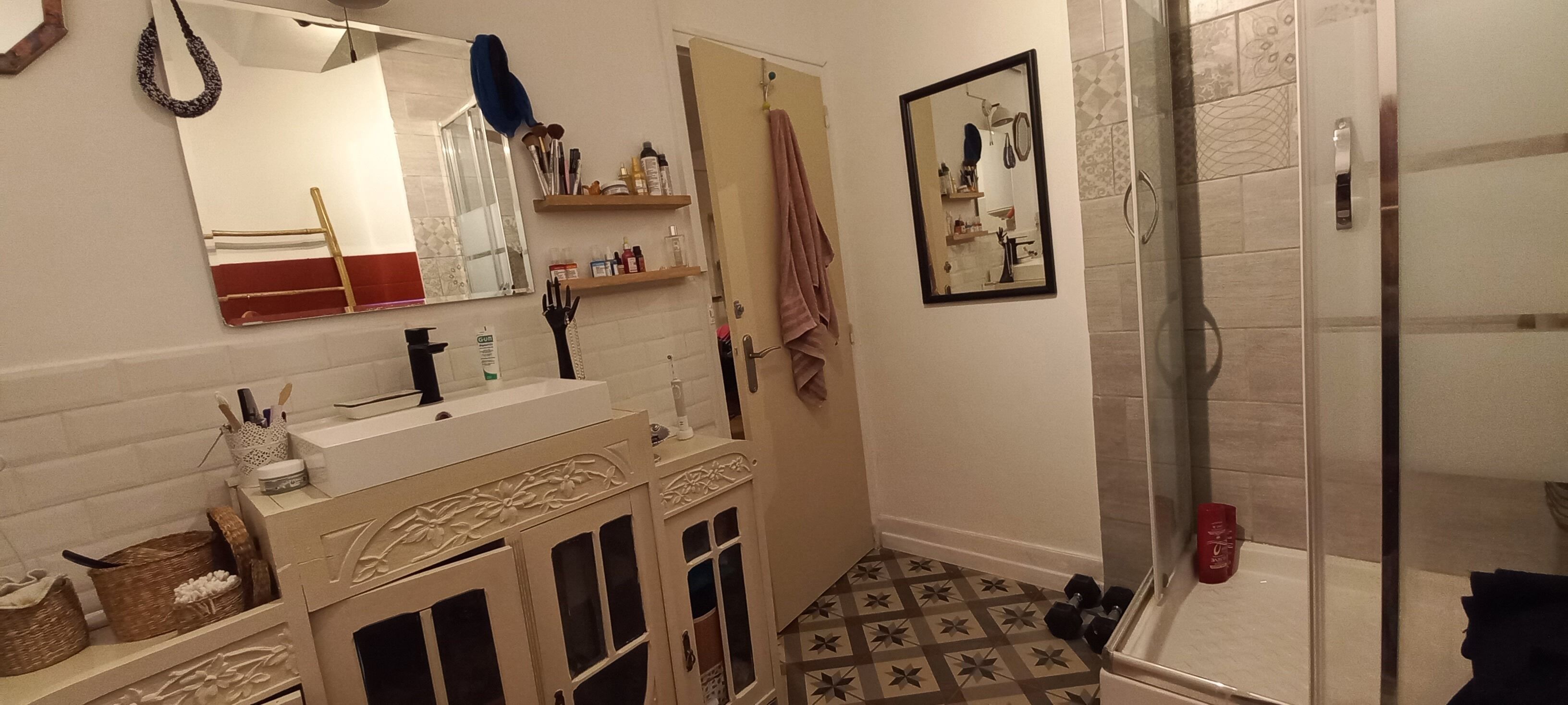 Une salle de bain comprenant un lavabo, un miroir, des étagères avec des articles de toilette, un espace douche et des carreaux de sol à motifs.