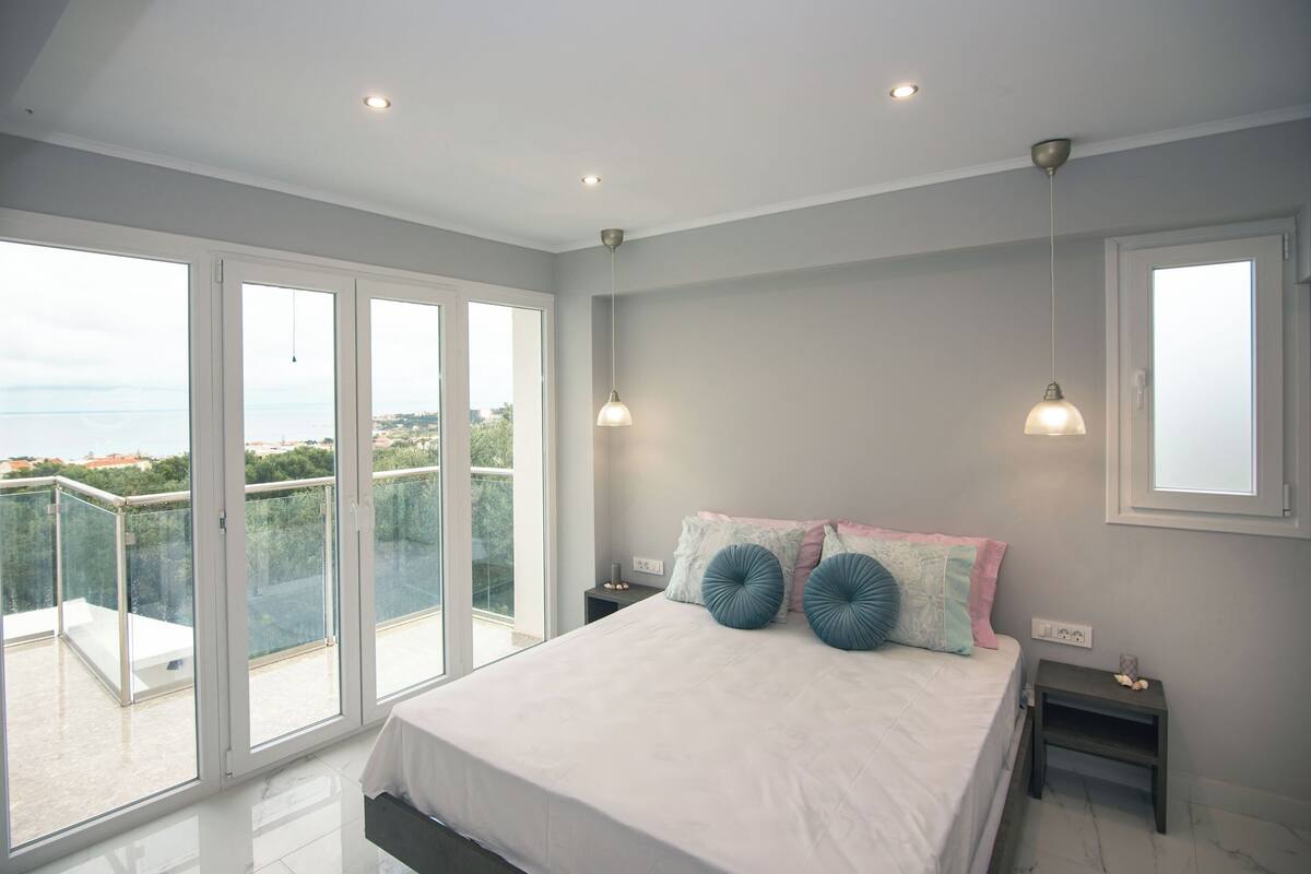 A bedroom with a large bed, two bedside tables, a nightstand, and a view of the outdoors through a sliding glass door.