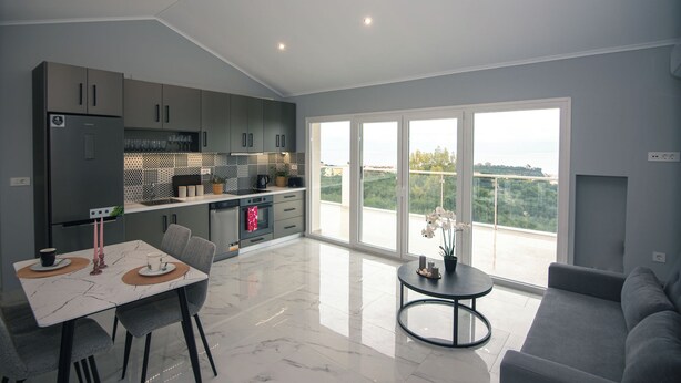 Una cocina moderna con armarios grises, un comedor con mesa blanca y un sofá gris.