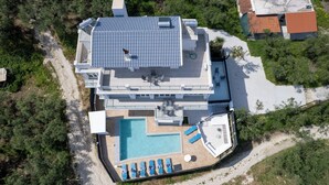 Un edificio moderno de dos pisos con piscina en la azotea, asientos exteriores y una vista despejada del paisaje circundante.