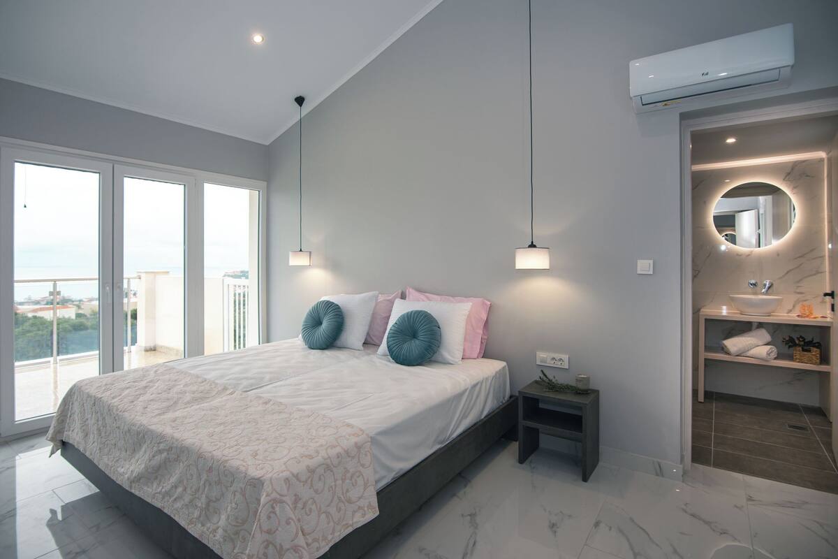 A modern bedroom with a large bed, bedside tables, a built-in wardrobe, and a bathroom with a sink and mirror.