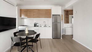 A modern kitchen with white cabinets, a stainless steel refrigerator, a dining table with chairs, and a wooden floor. - Chic 2 Keren Hayesod (Jerusalem)