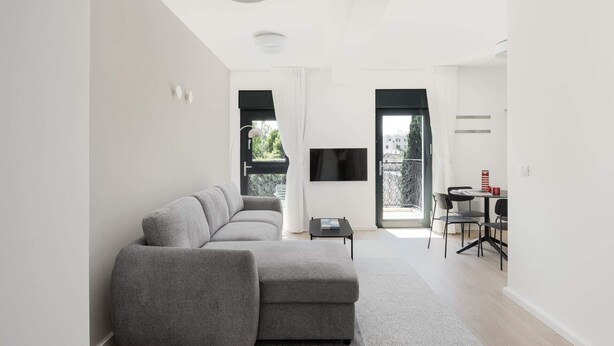 A modern living room with a grey sectional sofa, a small table, and a TV mounted on the wall. - Chic 2 Keren Hayesod (Jerusalem)