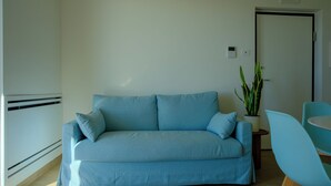 A living room with a light blue sofa, a small round table, and a potted plant. - IRIS Aurora Apartments (Baia Azzurra-levagnole)