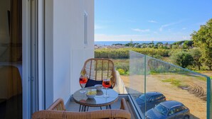 A balcony with wicker chairs, a glass table, and two drinks. A car is parked outside. - IRIS Aurora Apartments (Baia Azzurra-levagnole)