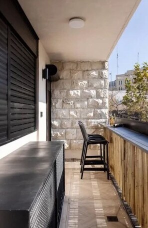 Un balcón con muro de piedra, barandilla de madera, una silla y una mesa negros.