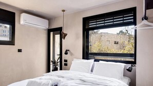 A modern bedroom with a large bed, an air conditioning unit, a window with blinds, and a view of the outside. - Luxury Mamilla view - Three Bedroom Apartment, Sleeps 8 (Jerusalem)