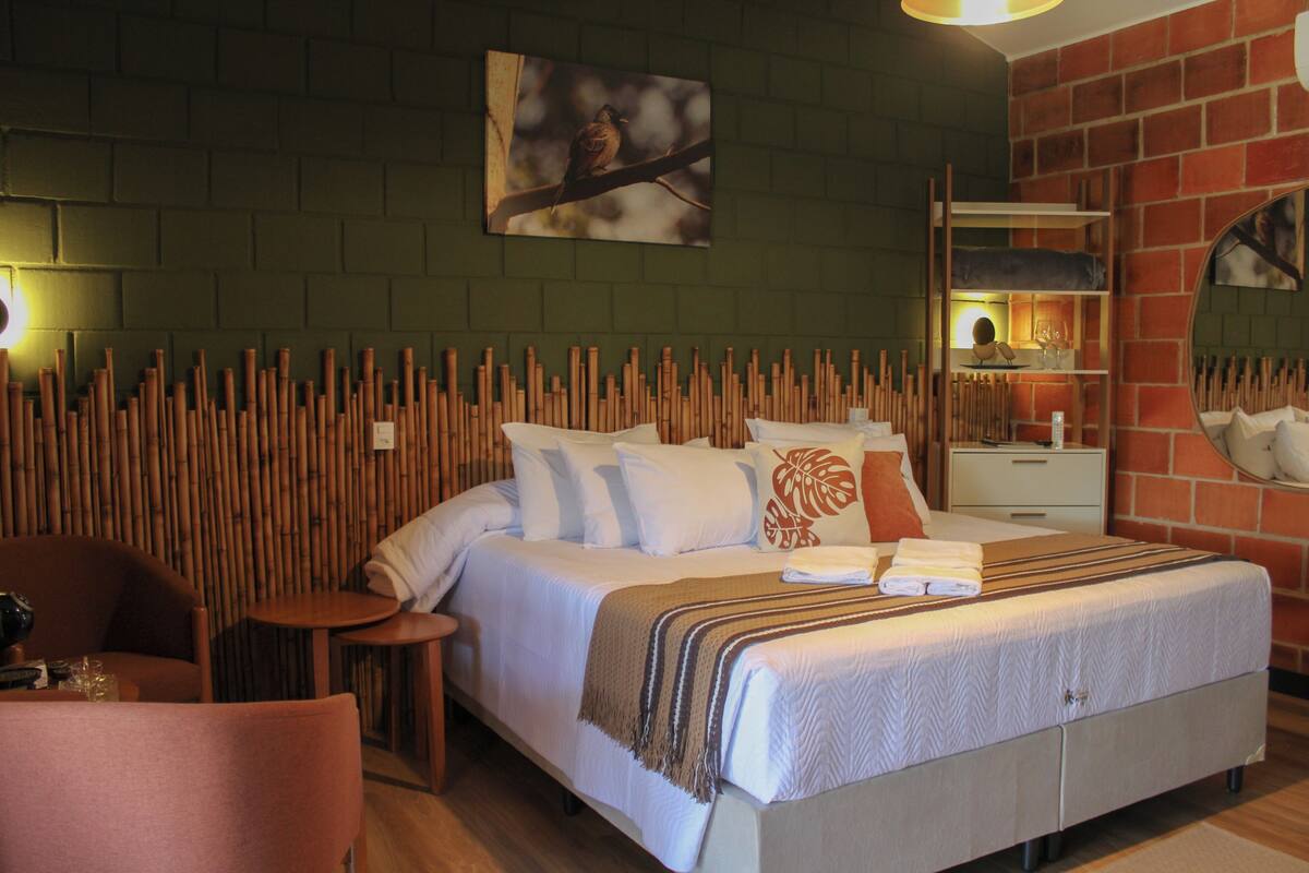 Ein Hotelzimmer mit einem Bett, einem Sessel, einem kleinen Tisch, einem Nachttisch und einem Spiegel.