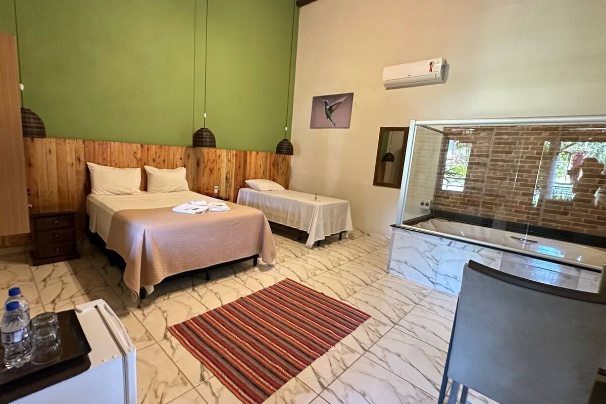 Ein Hotelzimmer mit zwei Betten, einem kleinen Tisch mit einer Flasche, einem roten Teppich, einer Duschkabine und Blick ins Freie.