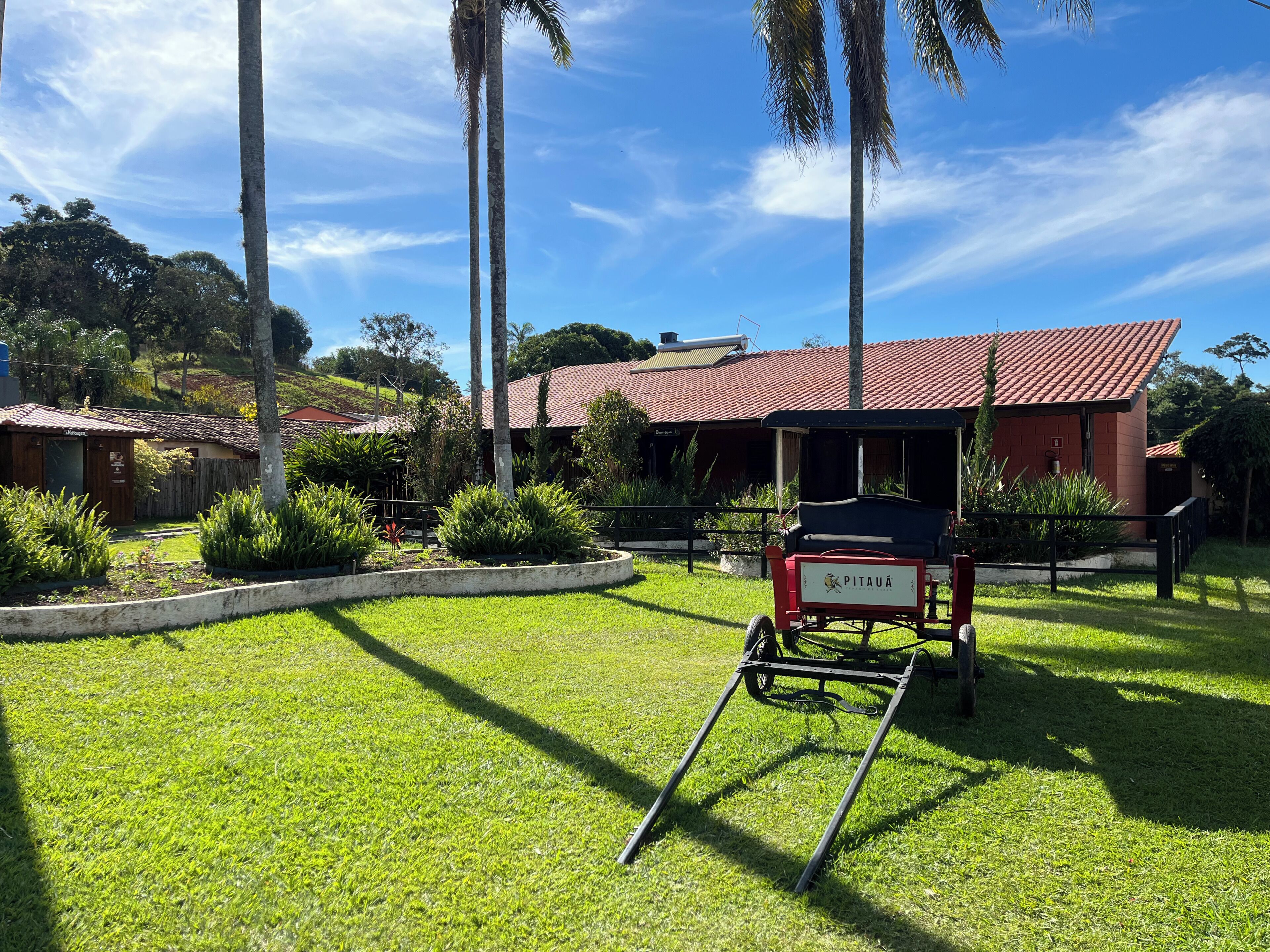 A well-maintained grassy area with a cart labeled 'PITAUÁ' in front of a building with a red roof.
