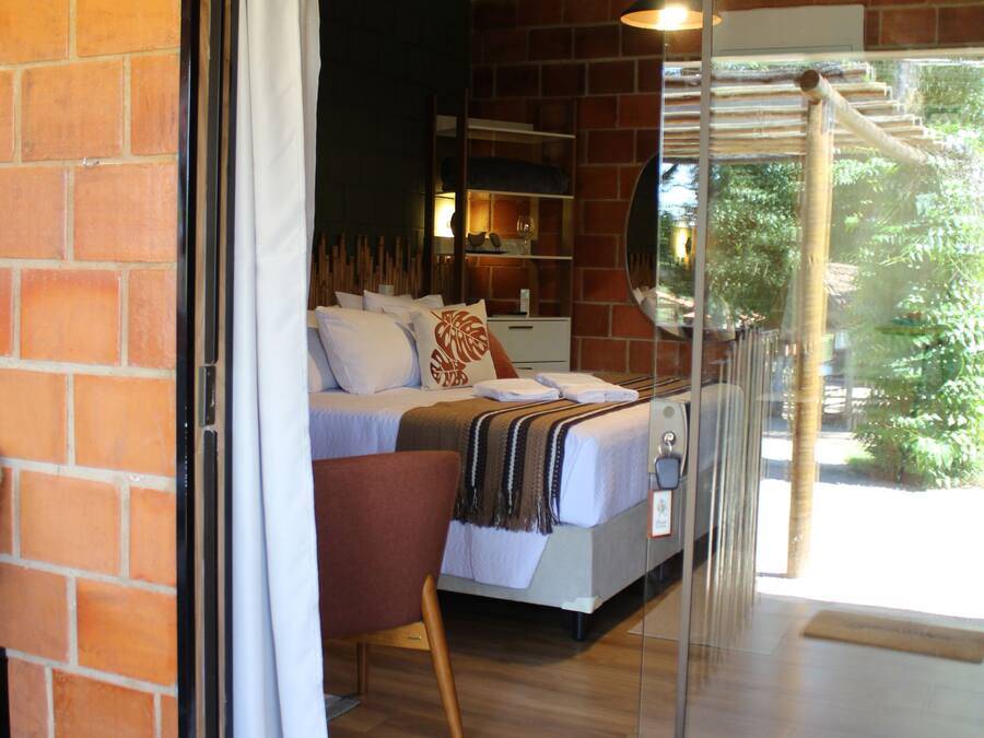 A bedroom with a bed, a chair, a bedside table, and a window with a view of greenery.