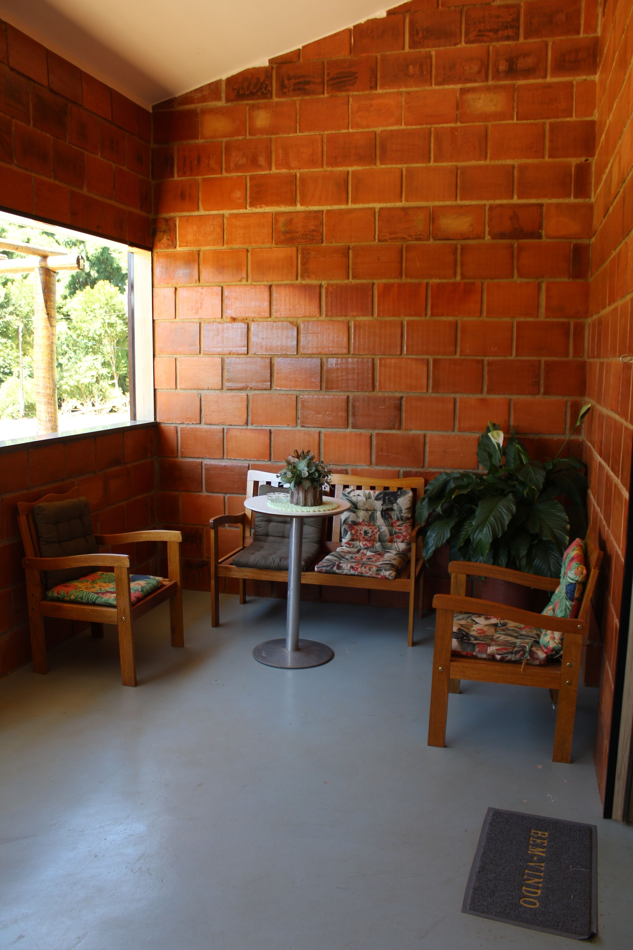 Ein Eckzimmer mit Backsteinwänden, einem runden Tisch, zwei Stühlen und einem Blumentopf.