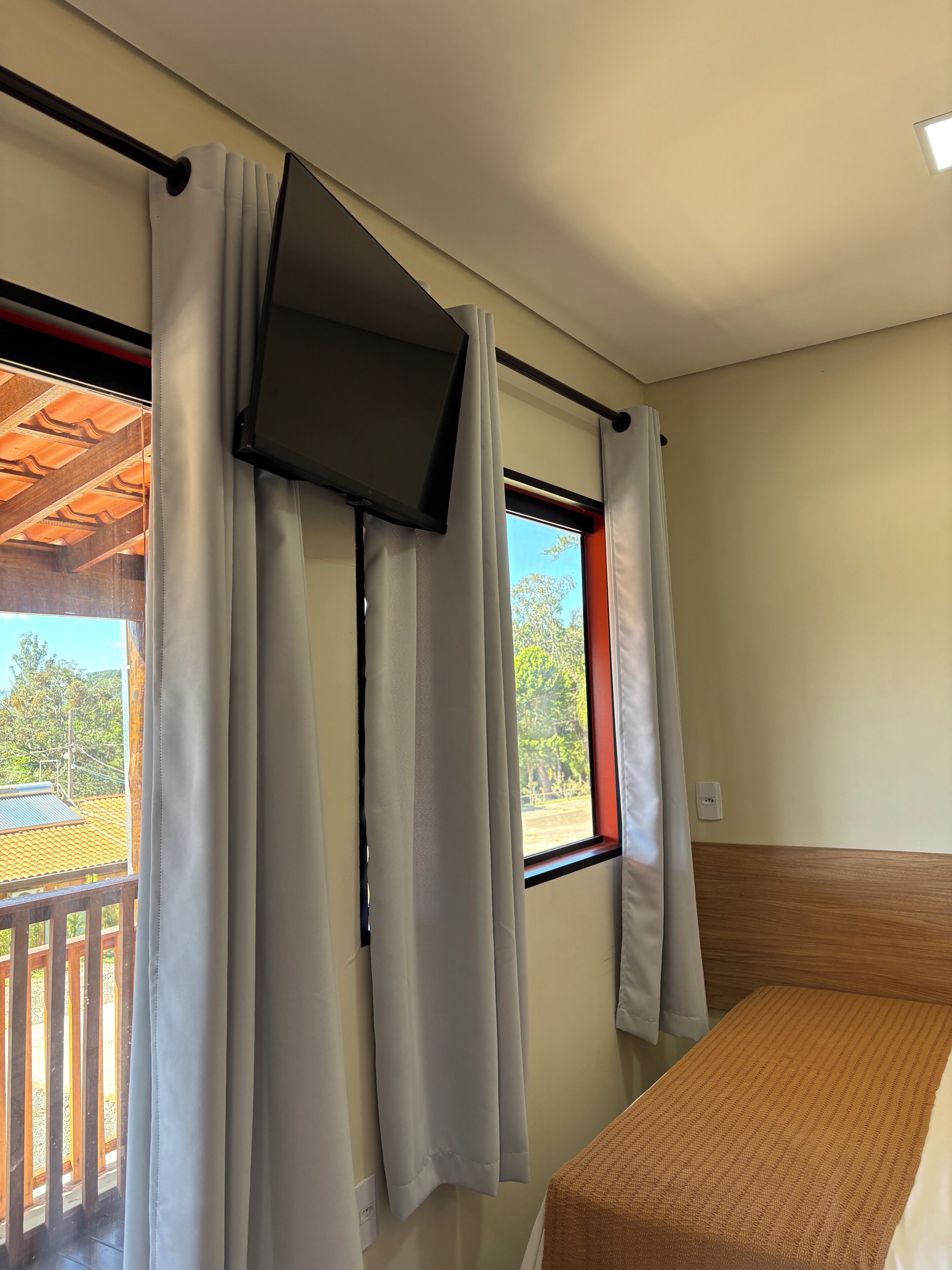 Una habitación con cama, ventana con cortinas, televisor montado en la pared y vistas al exterior.