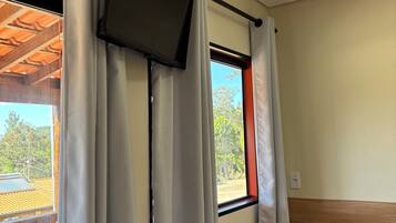 Una habitación con cama, ventana con cortinas, televisor montado en la pared y vistas al exterior.