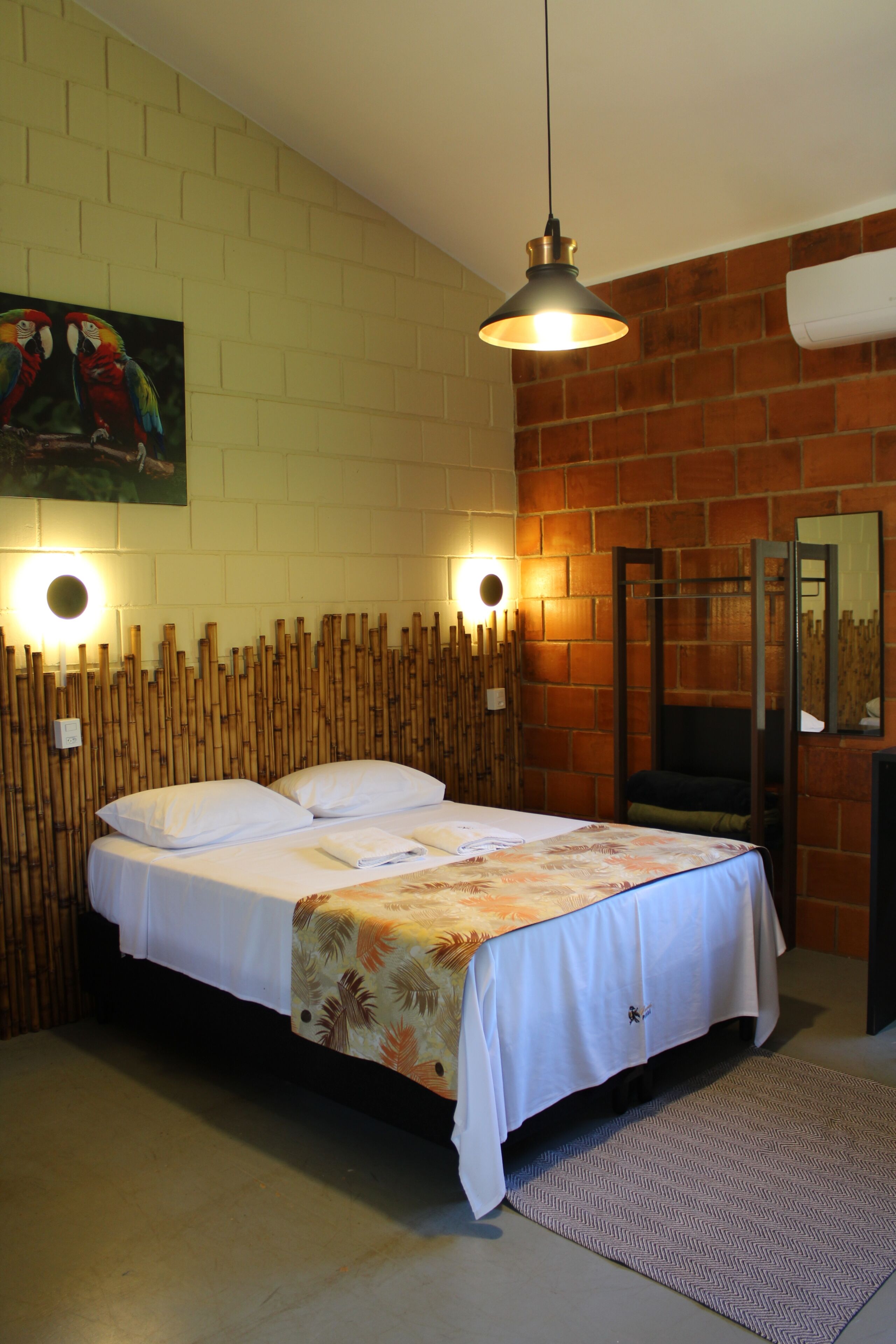 A room with a bed, a hanging light fixture, a wall-mounted air conditioner, and a painting.