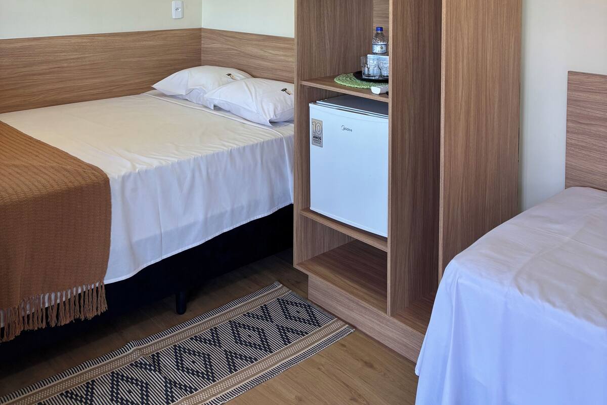 Ein Zimmer mit zwei Betten, einem Holzschrank, einer Minikühlschrank und einem gemusterten Teppich.