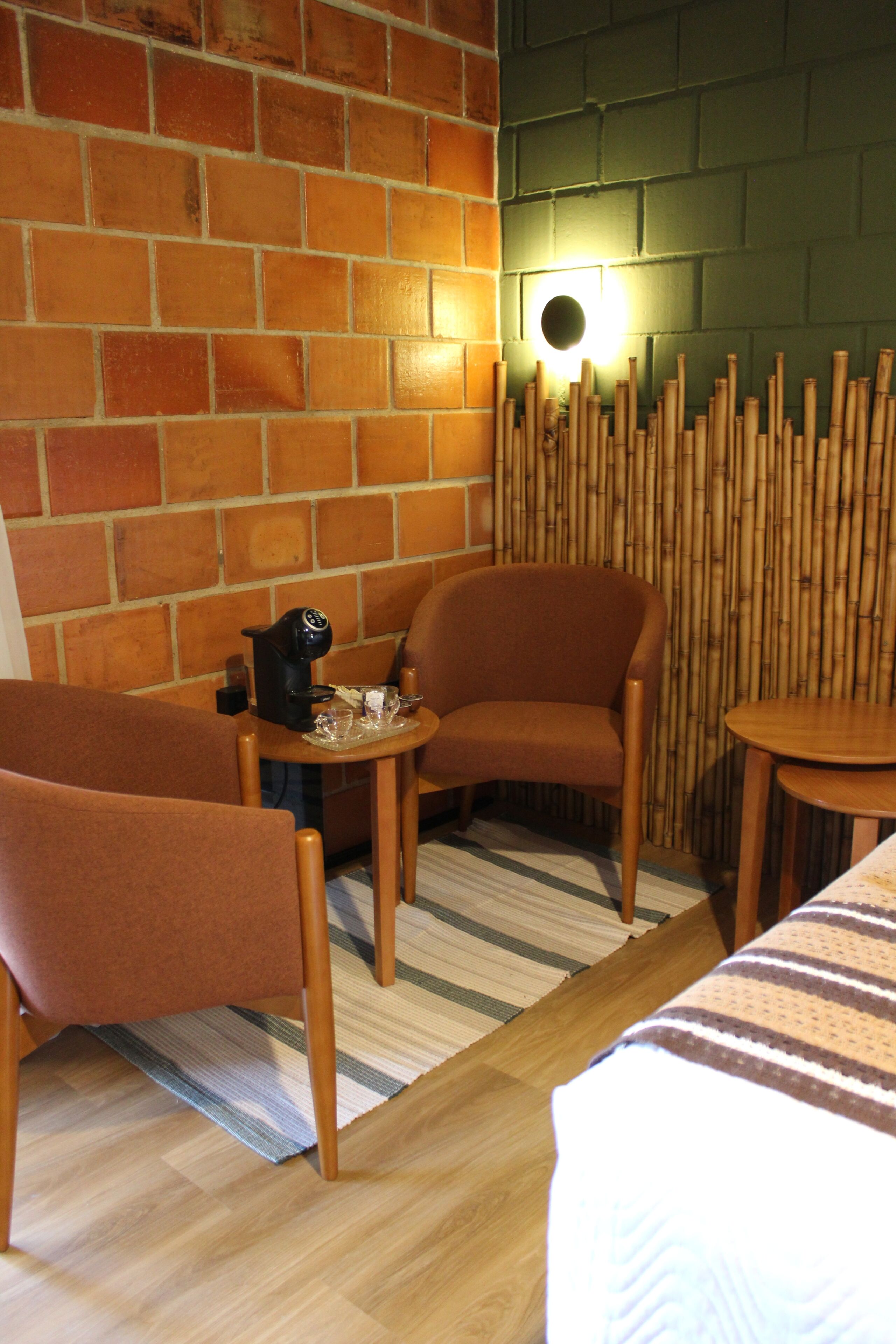A room with a brick wall, a bamboo screen, a small table with a kettle, and two chairs.