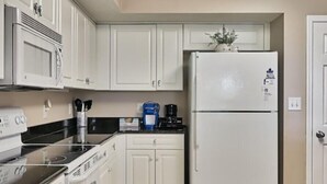 Une cuisine avec des meubles blancs, un four à micro-ondes, une cuisinière, un réfrigérateur et une machine à café.