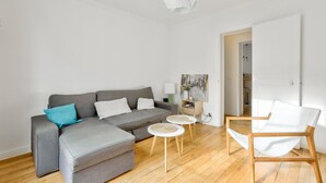 A modern living room with a grey sectional sofa, a white armchair, and a small round table. - Cozy apartment in the 11th arrondissement (Paris)