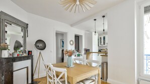 A modern kitchen with white cabinets, a wooden dining table, and white chairs. - Cozy apartment in the 11th arrondissement (Paris)