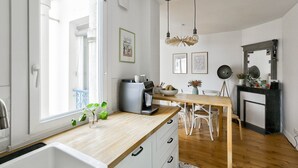 A modern kitchen with a wooden countertop, white cabinets, and a large window. - Cozy apartment in the 11th arrondissement (Paris)