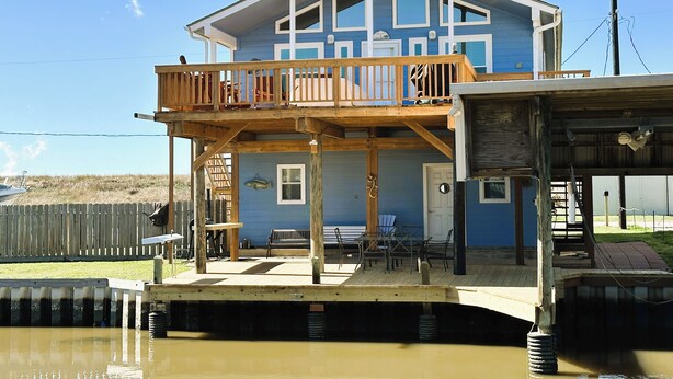 A two-story house with a balcony, a dock extending into a body of water, and a small outdoor seating area. - Fishing Haven at Linda's Mermaid Cove (Freeport)
