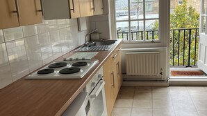 A modern kitchen with wooden cabinets, a built-in oven, a washing machine, and a large window with a view of the city.
