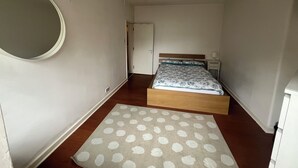 A bedroom with a bed, a bedside table, a nightstand, a round mirror, and a polka dot rug.