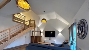 Ein modernes Wohnzimmer mit einer Holztreppe, einem blauen Sofa, einem Flachbildfernseher und einer großen Wanduhr.