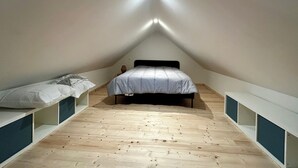 Ein kleines, dreieckiges Schlafzimmer im Dachgeschoss mit einem Einzelbett, integrierten Regalen und einer geneigten Decke.