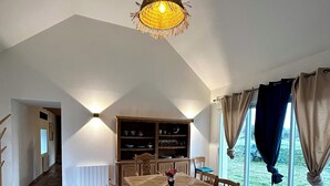 Ein Essbereich mit Holztisch und Stühlen, einer Hängeleuchte und Blick ins Freie durch große Fenster.