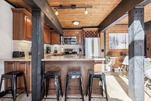 Una cocina con armarios de madera, un refrigerador de acero inoxidable y una isla central con taburetes.