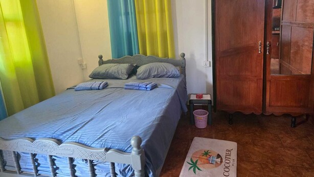 Een slaapkamer met een bed, een houten kledingkast en een klein tafeltje met een handdoek.