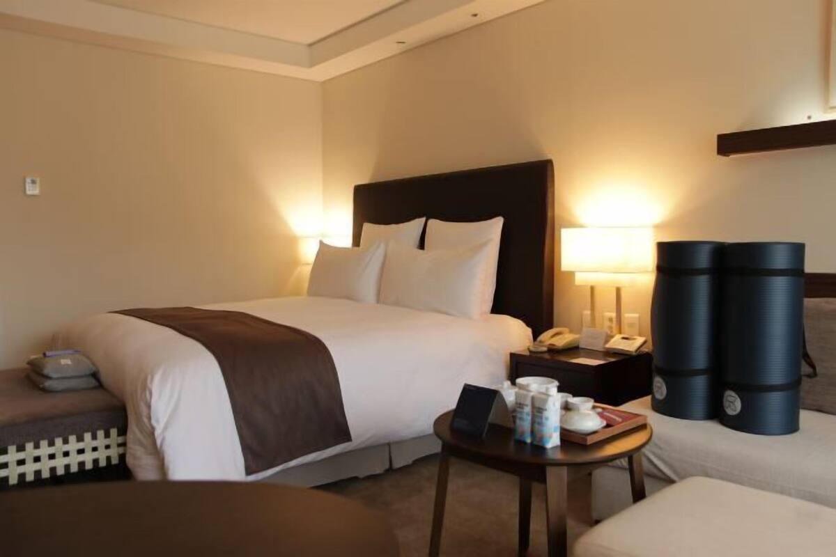 Ein Hotelzimmer mit einem Bett, Nachttisch, Lampe und einem kleinen Tisch mit Gegenständen darauf.