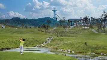 A golf course with a water hazard, a person in a yellow shirt, and a lighthouse in the background.