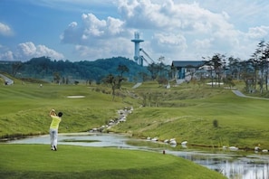 A golf course with a water hazard, a person in a yellow shirt, and a lighthouse in the background. - InterContinental ALPENSIA PYEONGCHANG RESORT by IHG (Pyeongchang-gun)