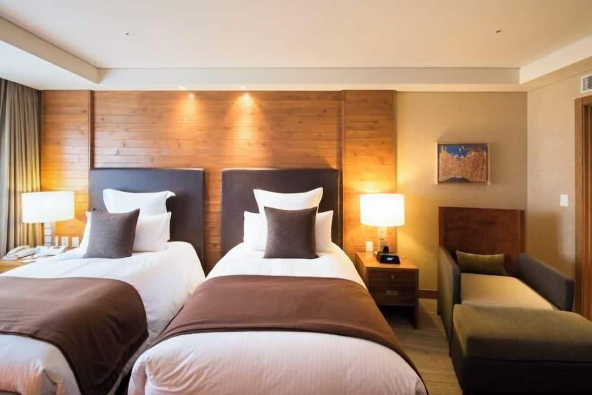 Ein Hotelzimmer mit zwei Betten, einer Couch, Holzwandverkleidung und einem Bild an der Wand.