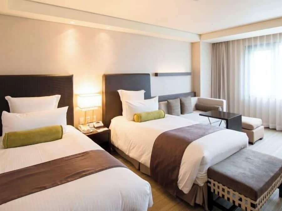 A hotel room with two beds, a sofa, a small table, and a window with curtains.