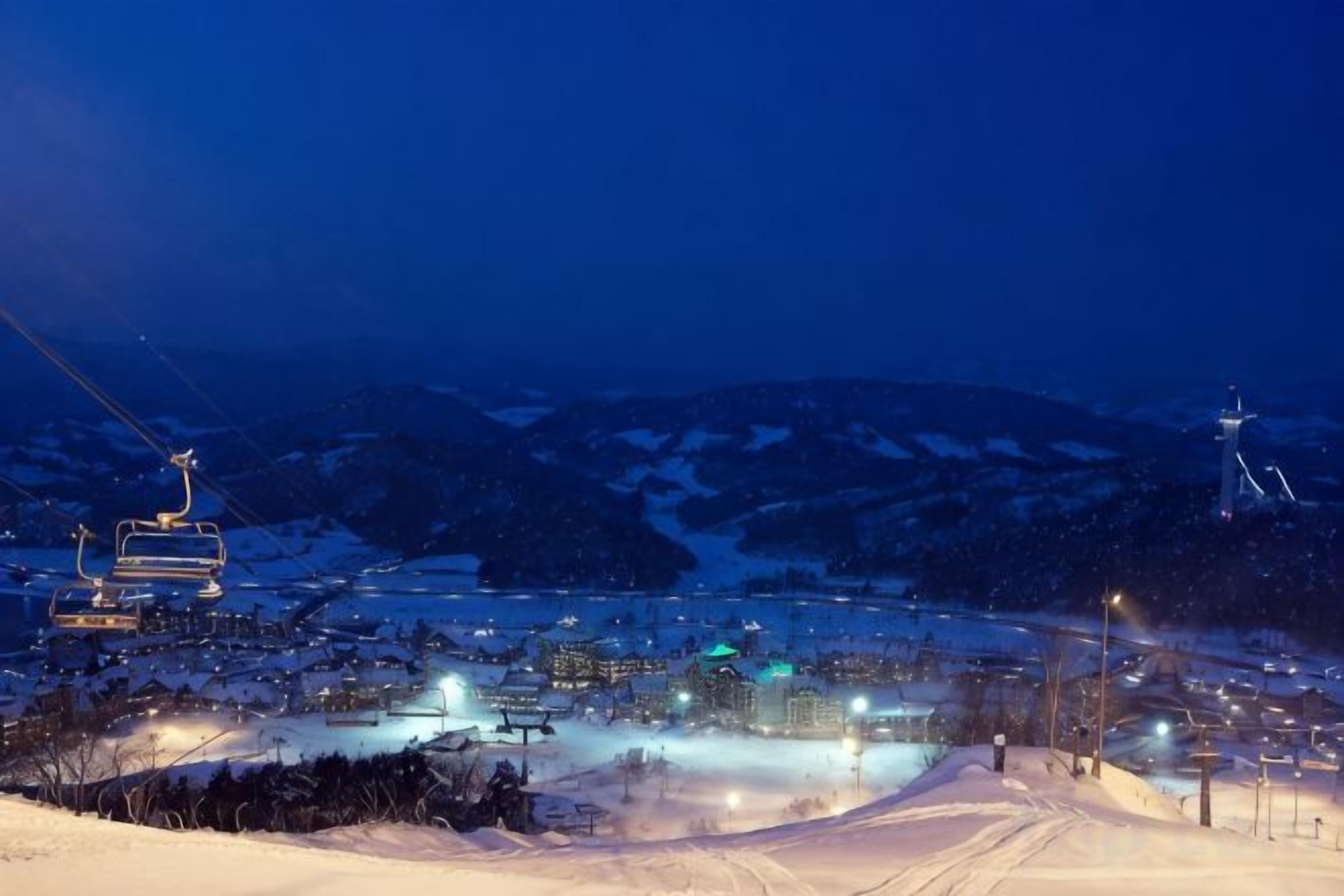 Un poble cobert de neu amb un remuntador d'esquí i edificis il·luminats.