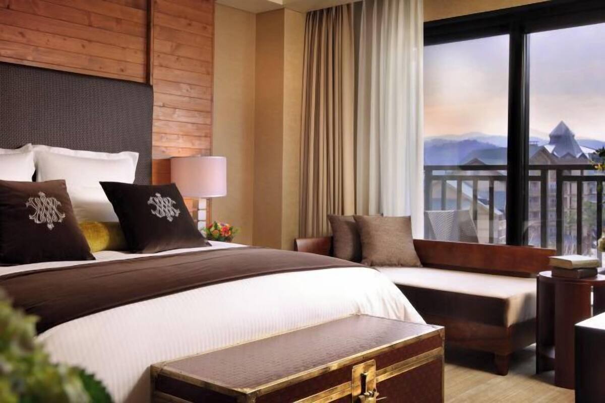 Ein Hotelzimmer mit Bett, einer Couch, einem hölzernen Kopfteil, einem großen Fenster mit Aussicht und einem Nachttisch mit Lampe.